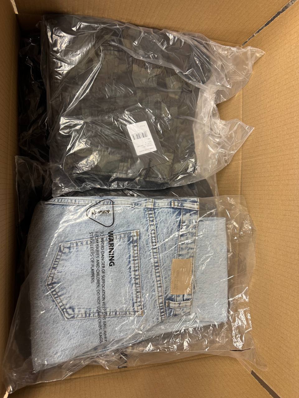 Geöffnete Bekleidungs-Mixkiste mit 25 gemischten Teilen, darunter eine hellblaue Jeans und dunkle verpackte Textilien